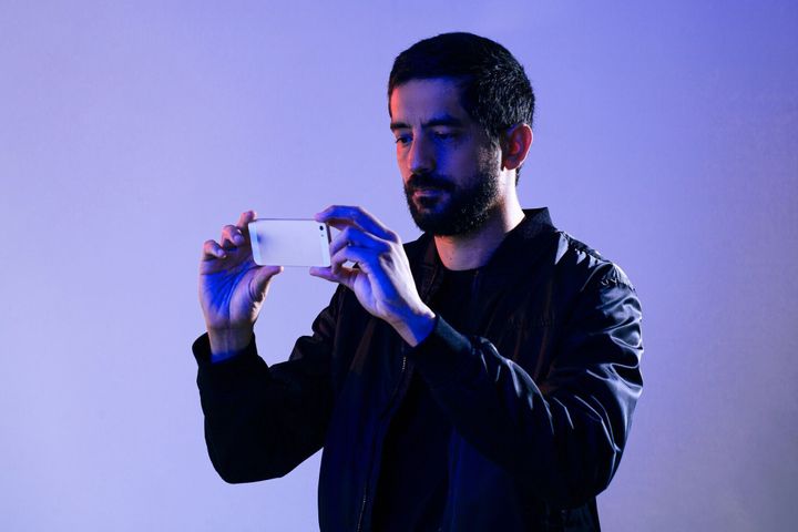 青と赤のライトで照らされたジャケットを着て携帯電話を持っている男。スマートフォンで警察を撮影する男の概念
