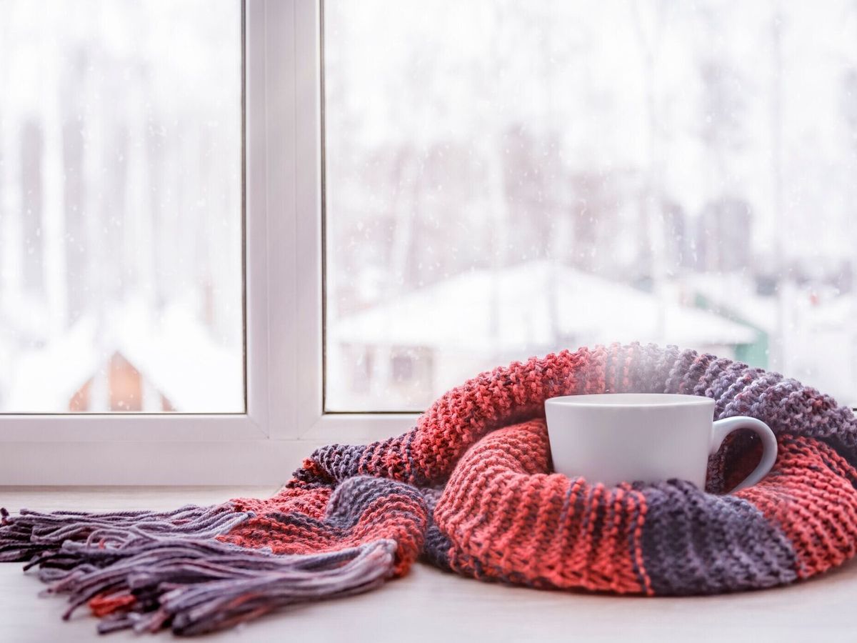 ニットのスカーフで温められた熱いお茶のカップは、冬の窓に対して窓辺にあります