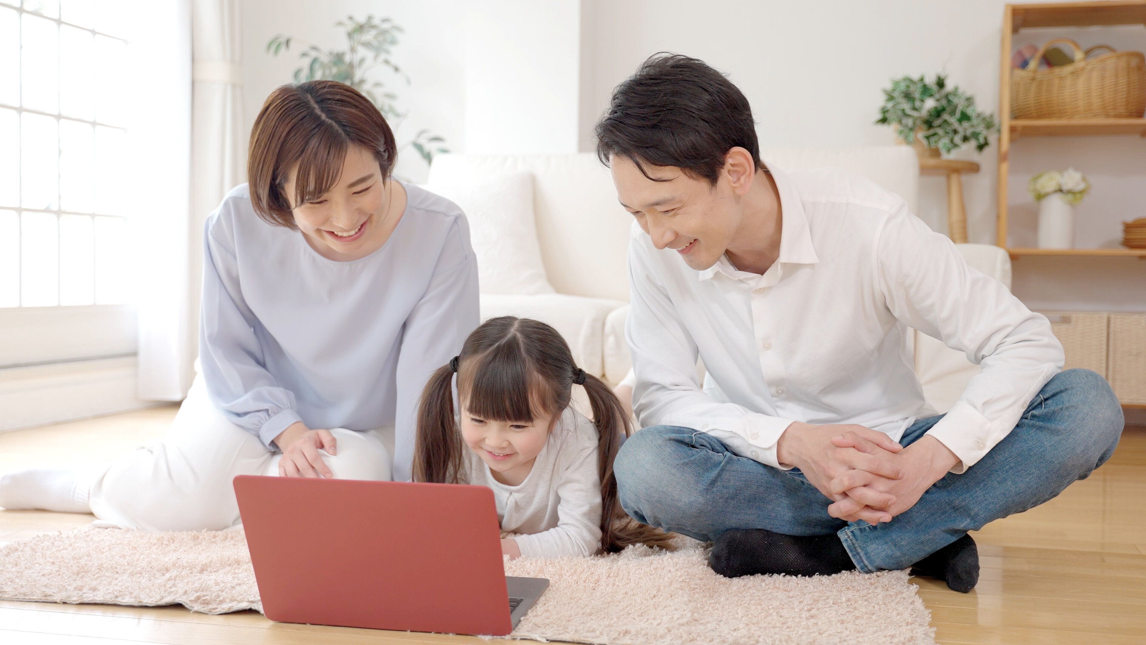 若いアジアの両親と娘は、リビングルームでラップトップを使用して