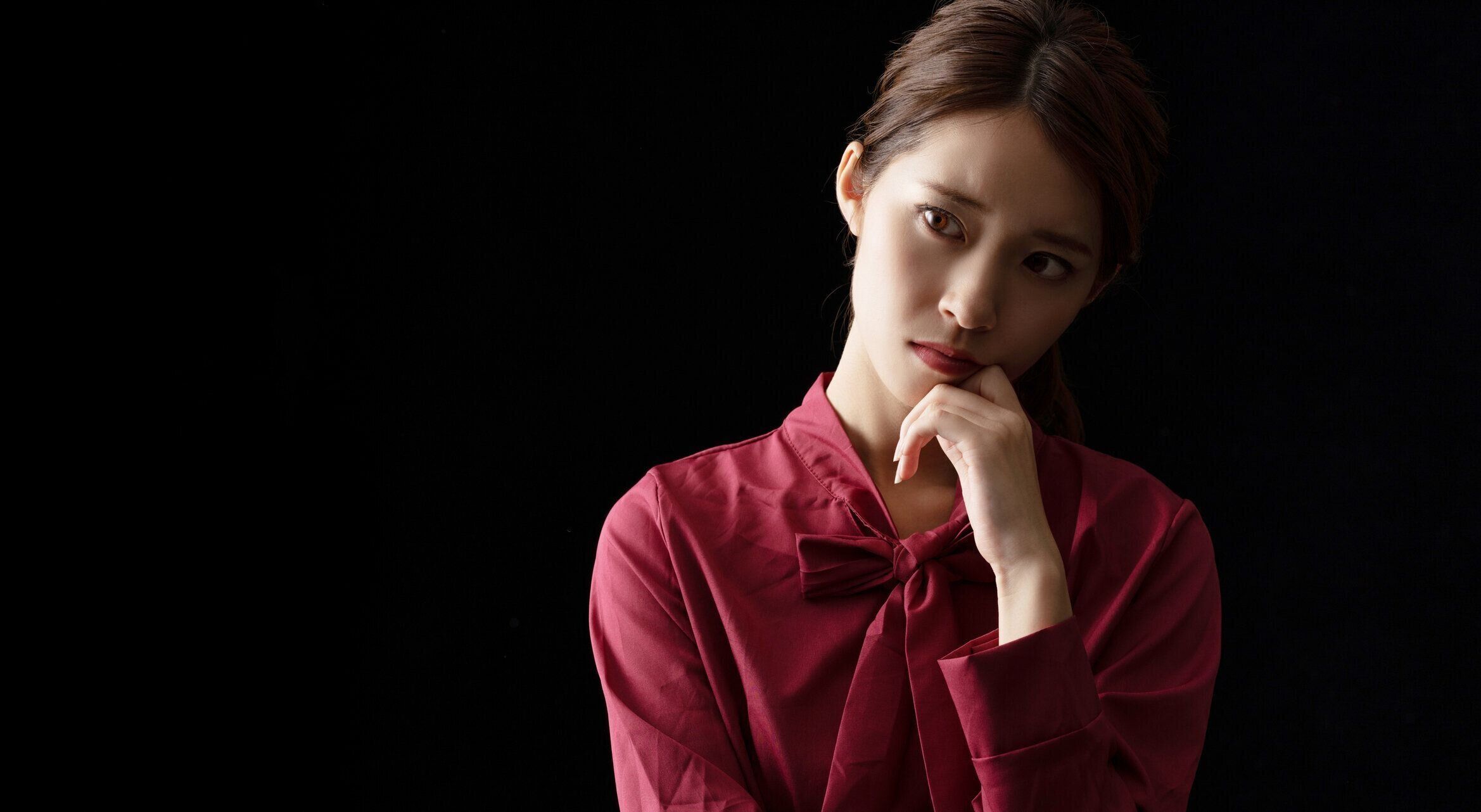 黒の背景に困ったアジアの女の子.