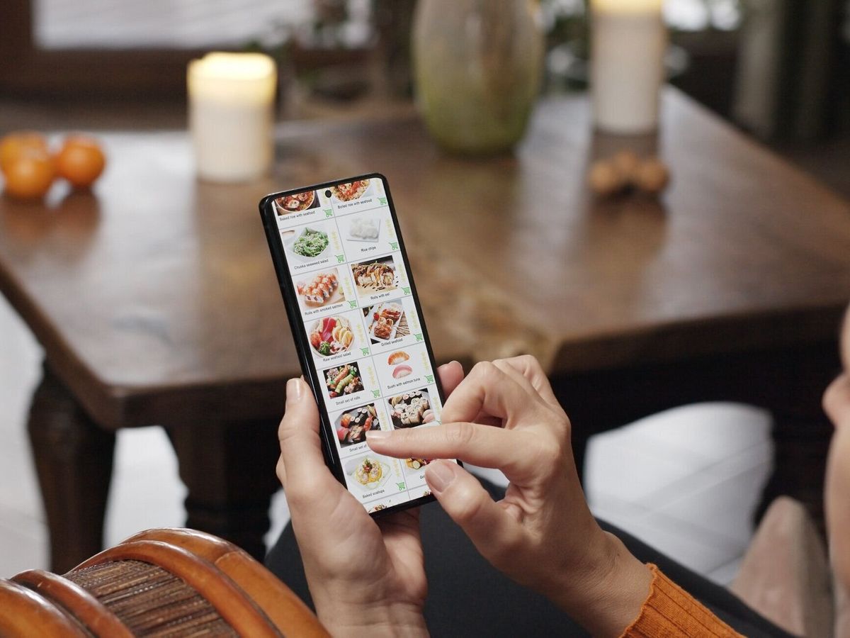 自宅でスマートフォンを使って食べ物を注文する。女性がスマートフォンのアプリを使って日本食レストランのインターネットメニューで寿司セットを選ぶ。暖炉の中で燃えている火のある�