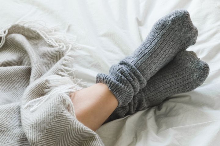 足が毛布の下ベッドの上灰色のソックスと交差