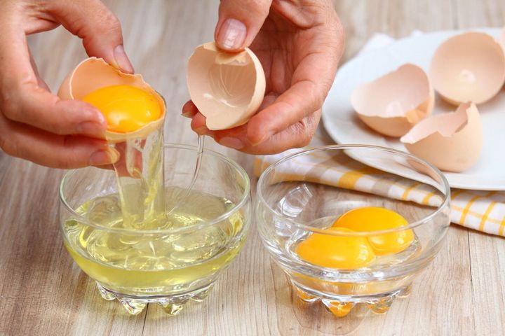 卵白と黄身を分けるために卵を壊す女性の手