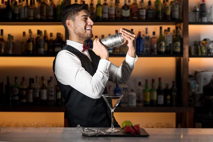 カクテルを作るクールなプロのバーテンダーは、カクテルシェーカーを振ります。モダンなバーでアルコール飲料を作る本格的なバーマン。