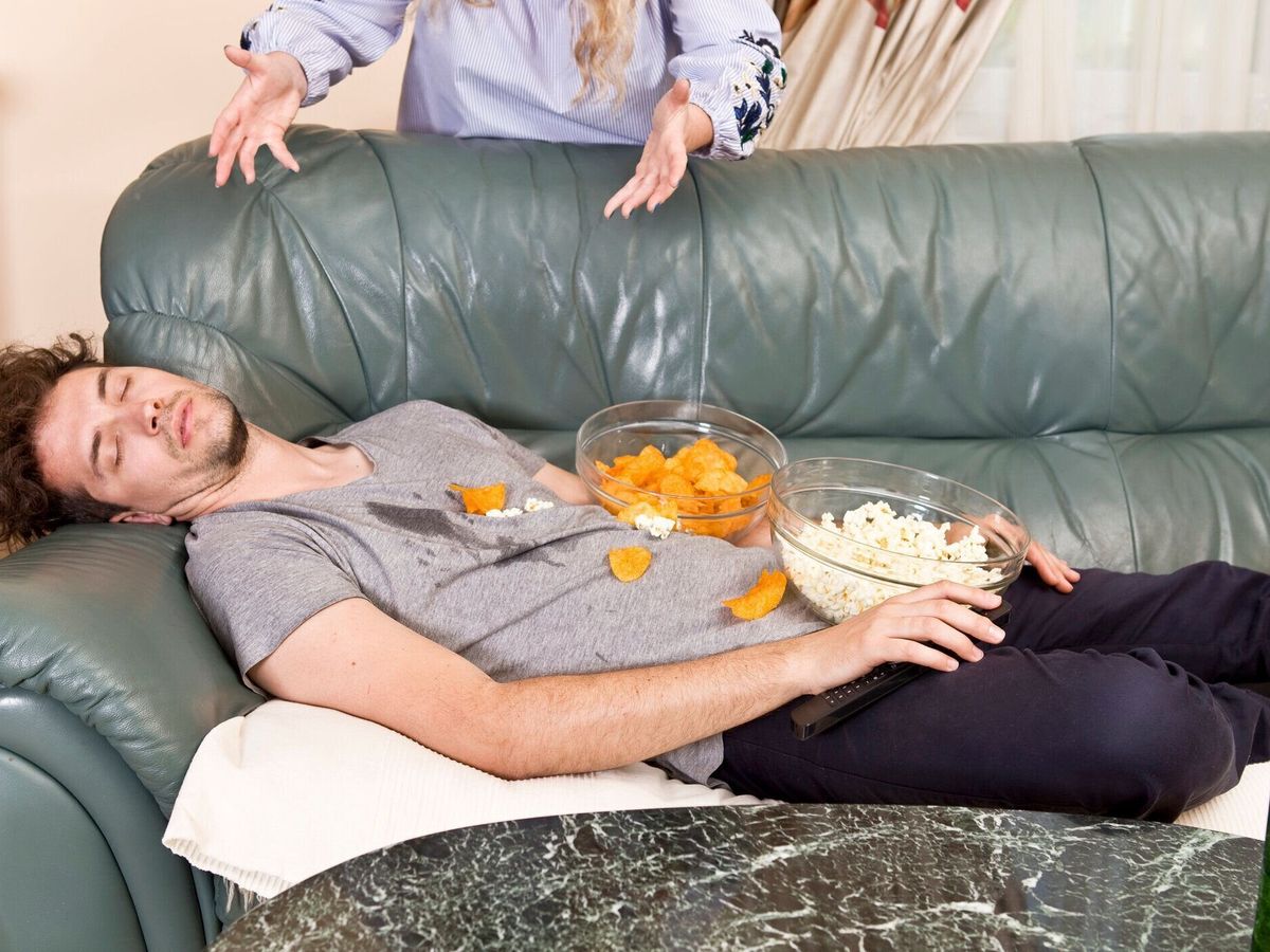 怒っている妻とソファとジャンク フードで眠っている夫
