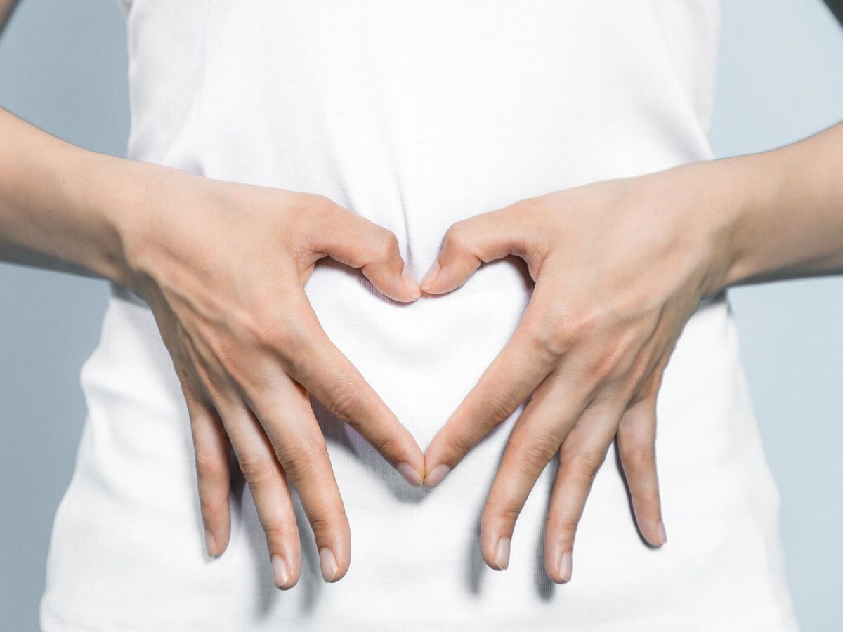 ハートの形を作る若い女性は彼女の胃に手します。