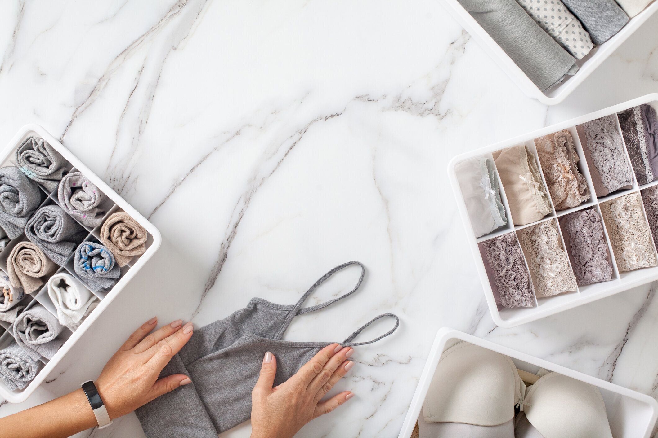 女性の手はきちんと下着を折りたたみ、白い大理石の背景に引き出しの主催者でソート