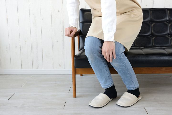 リビングルームで痛みを伴う膝を保持している女性