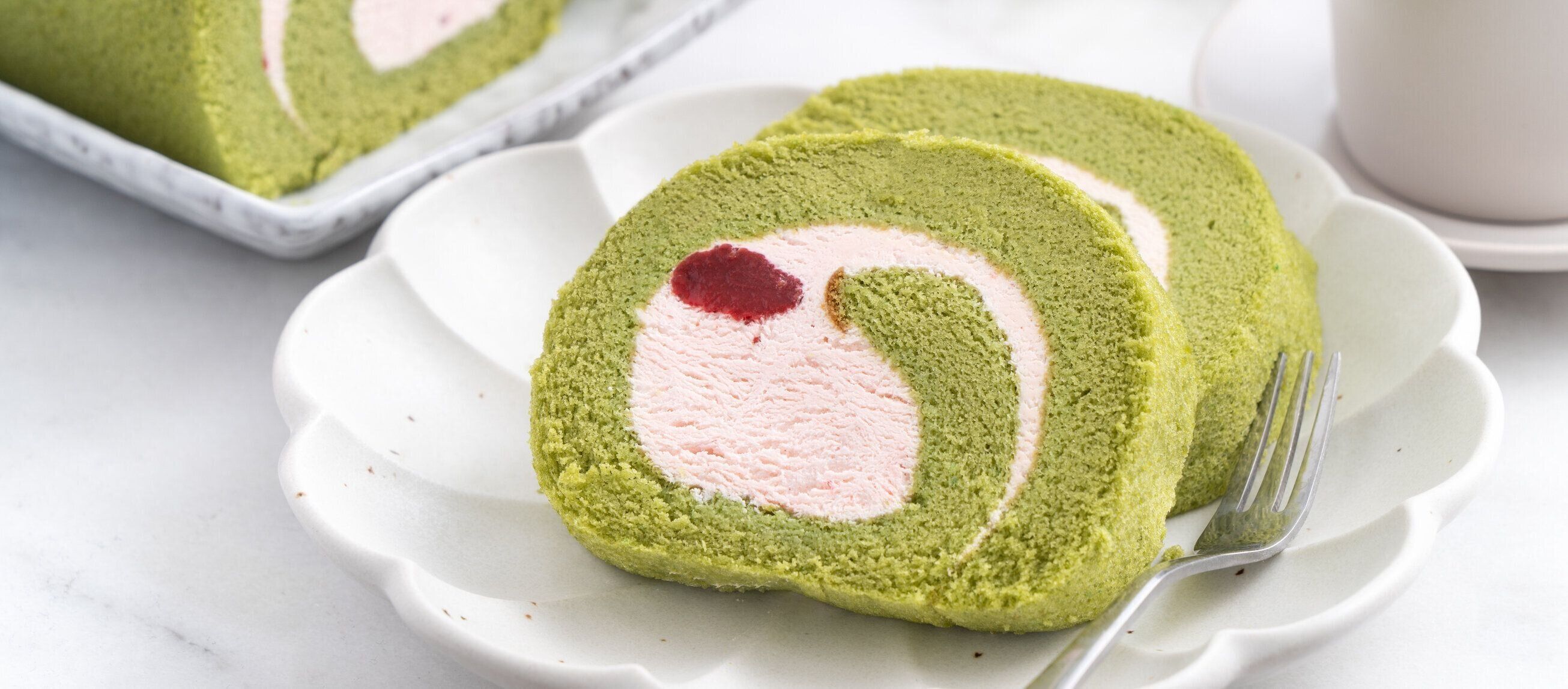 白い背景にイチゴクリームとおいしい抹茶スイスロールケーキスライス。