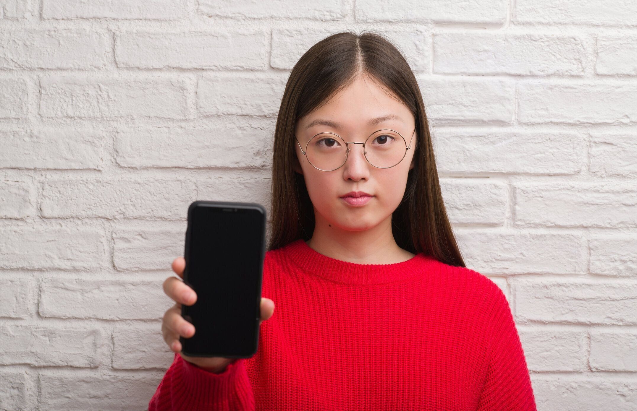 深刻な考えるスマートの顔に自信を持って式にレンガ壁表示スマート フォン上の若い中国の女性