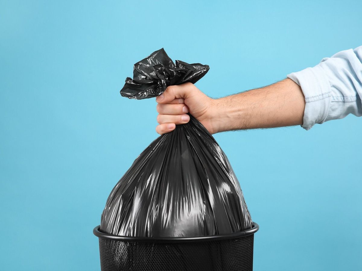 水色の背景にゴミ袋をゴミ箱から取り出す女性、クローズアップ