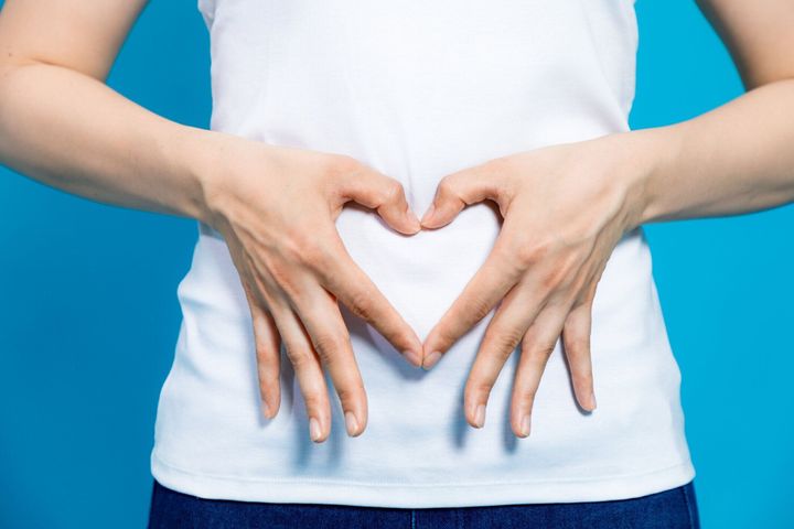 ハートの形を作る若い女性は彼女の胃に手します。