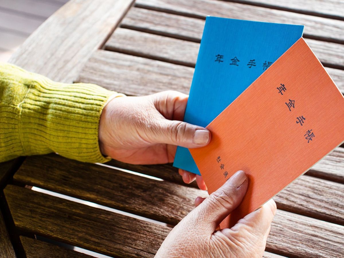 女性が手に持っている本のタイトルは「年金ハンドブック」です。