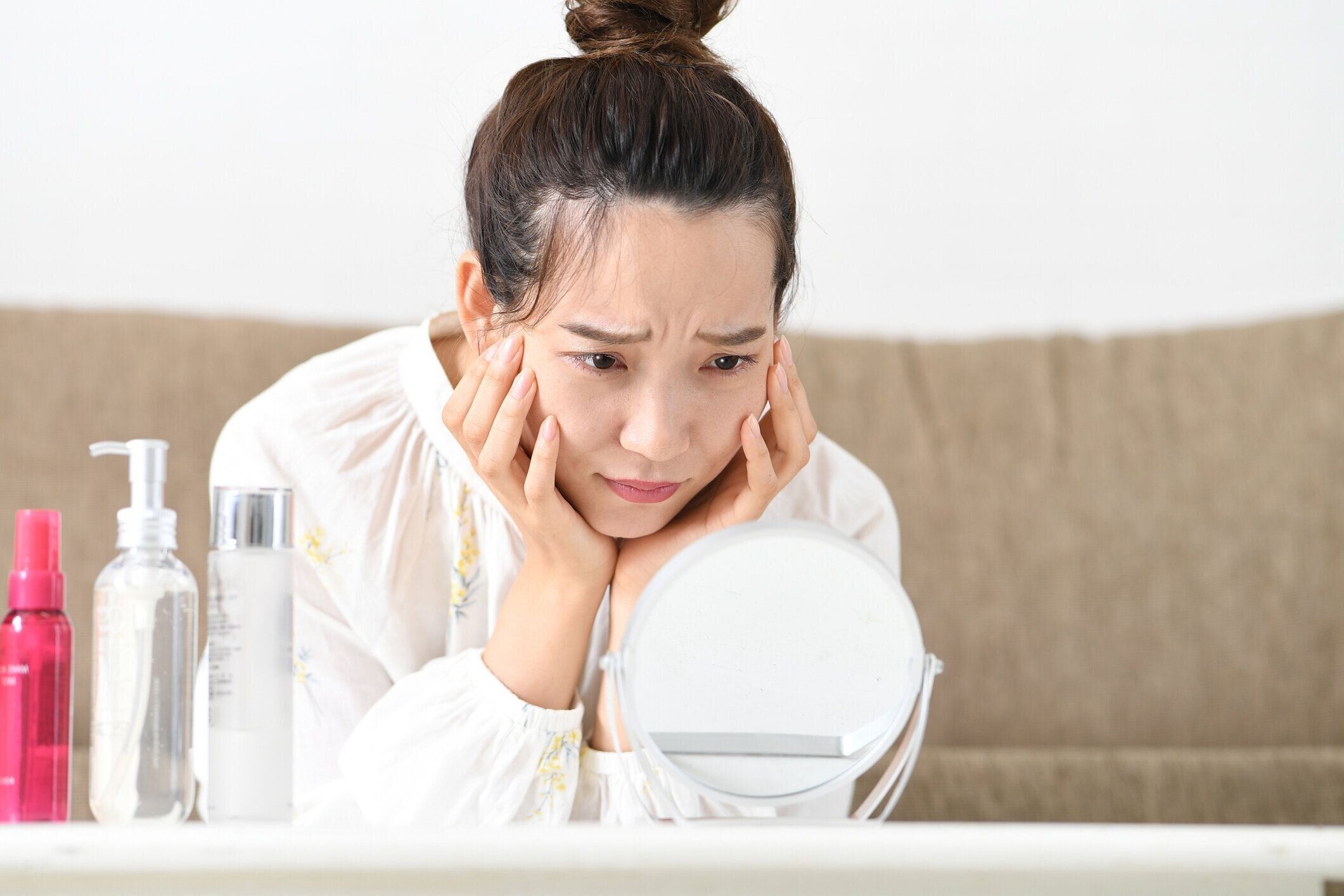 肌トラブルに悩むアジアの若い女性が鏡を見る