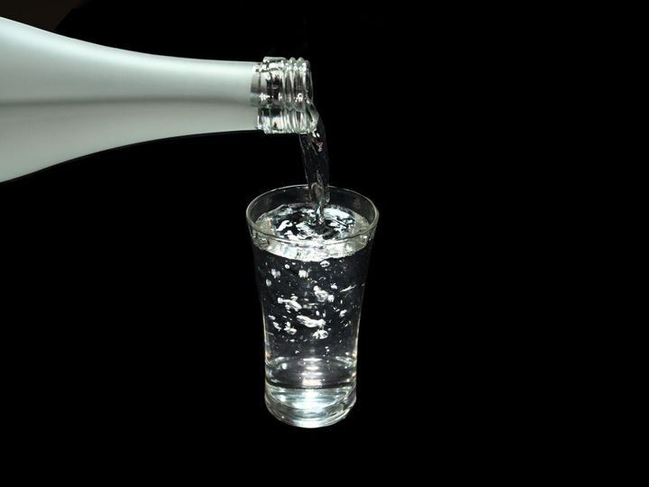 日本酒、米から作られたお酒、日本酒のボトルから黒い背景のショットグラスへ