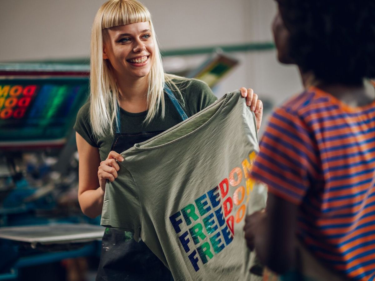 スクリーンプリントされたシャツをスーパーバイザーに見せる笑顔の印刷店員