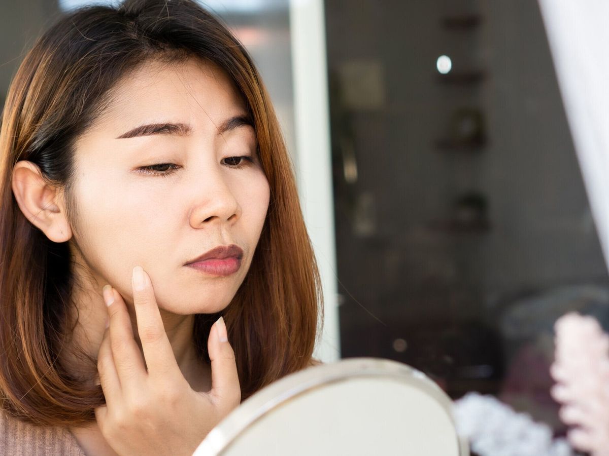 心配した顔で鏡に彼女の乾燥した、暗い色の唇をチェックするアジアの女性