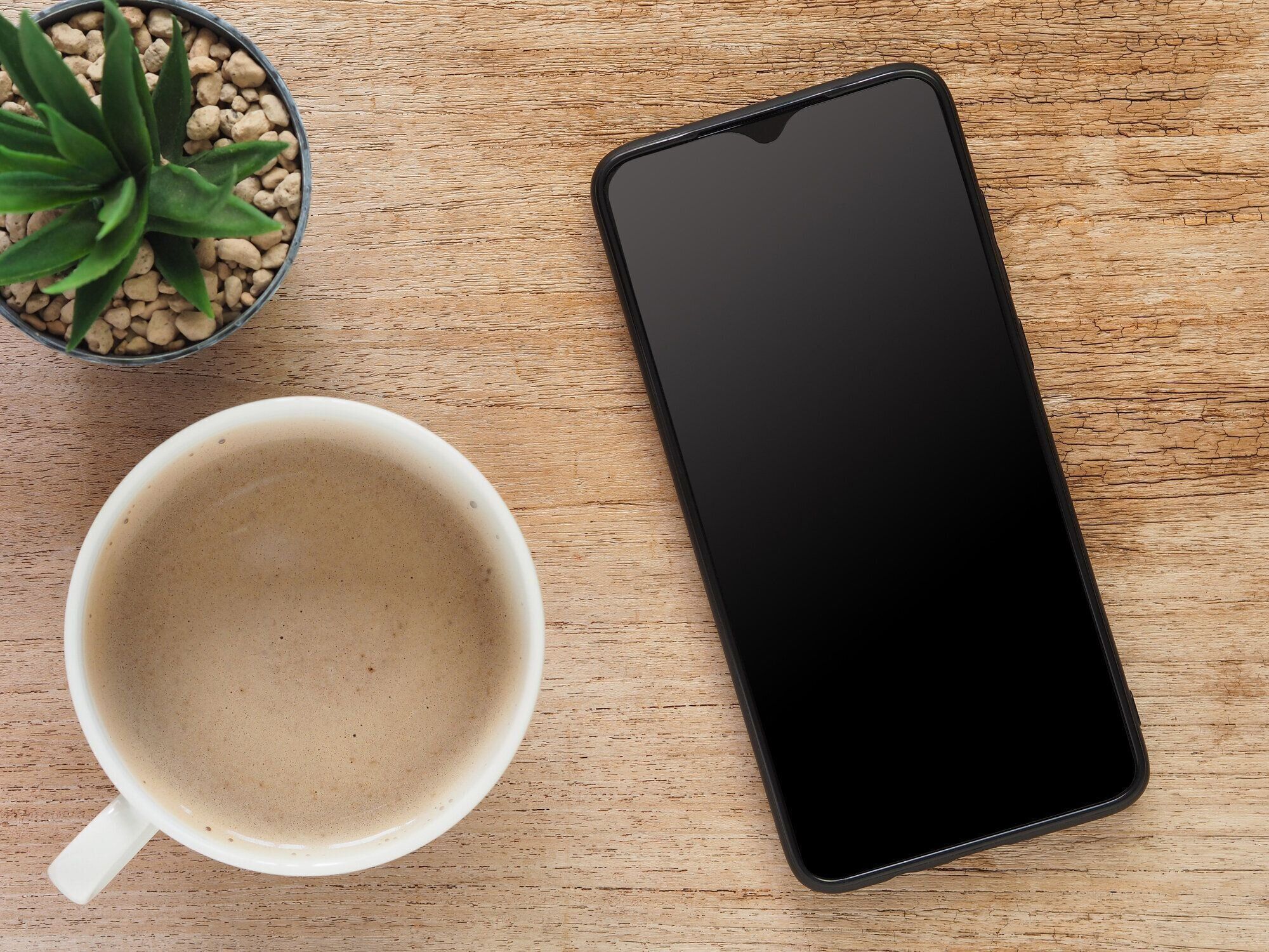 トップビュー、空白の画面とホットコーヒーカップ、素朴な木製のサボテンとスマートフォン。フラットレイ、あなたのテキストのためのスペース。