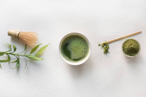 白いコンクリートのテーブルの上に儀式緑抹茶と竹の泡立て器。トップビュー。