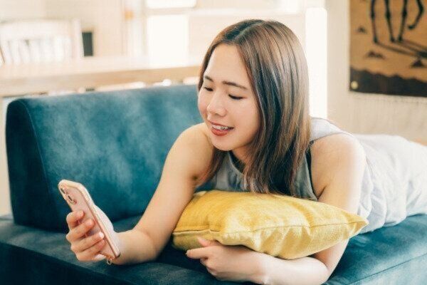 ソファに寝転びスマホでネットショッピングをする女性