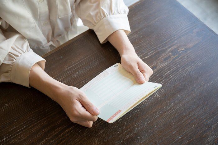 机の上で通帳を開こうとする若い女性
