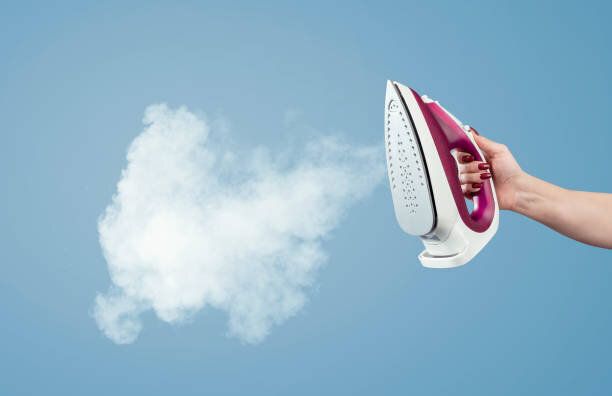 女性の手は青い背景に蒸気で鉄を保持します