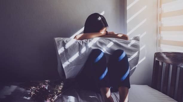 アジアの女性は、ベッドで自分の膝を抱いて座っています。悲しい気持ち、暗い寝室でブラインドを窓から日光愛の失望。ビンテージ トーン。