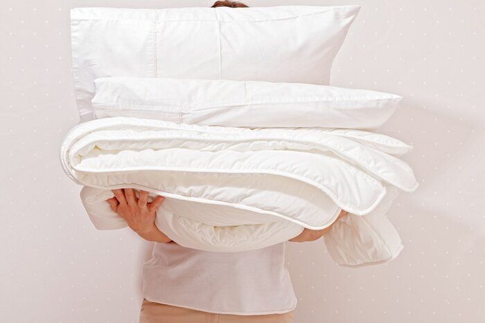 睡眠のための寝具の山を保持している女性。世帯