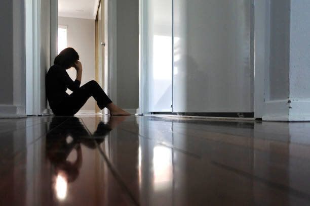 暗い家の廊下の床に座っている悲しい女性。