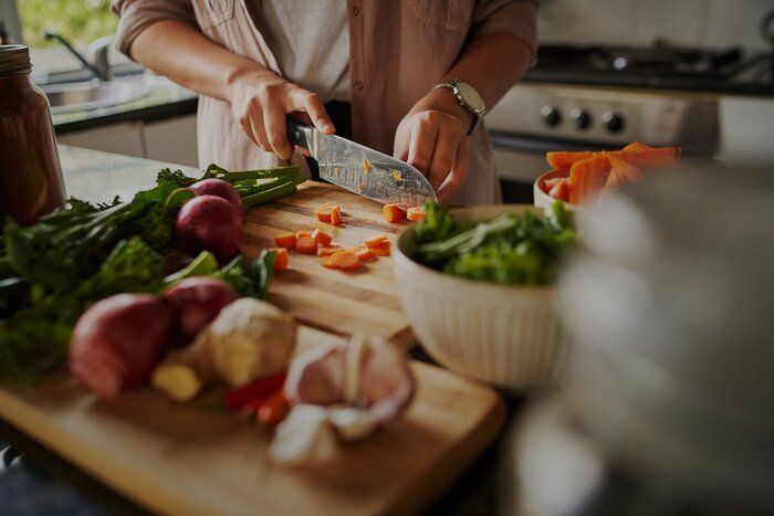 現代のキッチンにいる間、まな板に新鮮な野菜を刻む若い女性の手のクローズアップ - 免疫システムを高め、コロナウイルスを撃退するために健康的な食事を準備