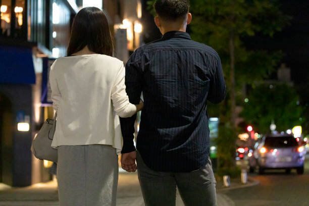 夜の繁華街で手をつないで歩く男女のバックビュー