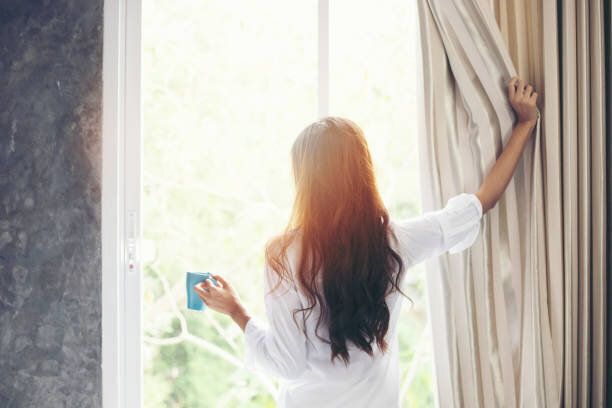 アジア女性を彼女のベッドでコーヒーとウェイク アップを完全に飲んで休んで、サンシャインに新鮮な空気を得るために朝のカーテンを開ける