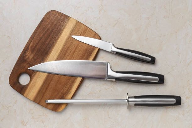 プロのシェフナイフ、剥離ナイフ、キッチンテーブルの上の木製のまな板の上の研ぎ鋼。シェフの作業ツール。モダンなキッチン用品。