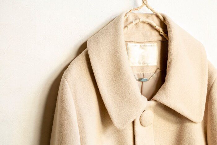 白い背景に服のハンガーにぶら下がるベージュのウールのコート