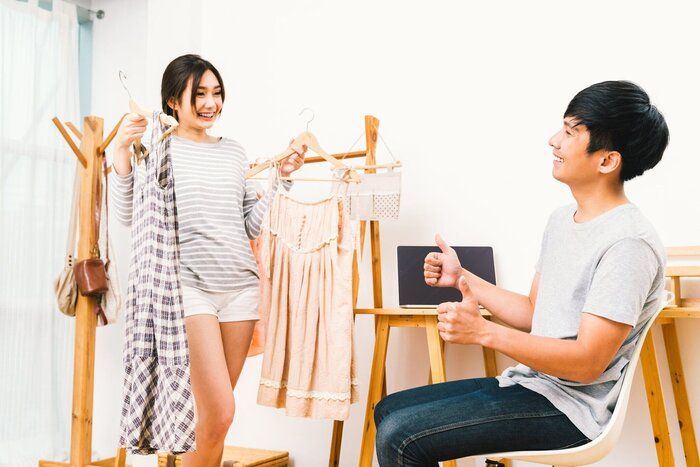 アジアの若い恋人カップルが家で一緒に布を選択します。ガール フレンド 2 ドレス、彼氏の親指を保持します。旅行や旅行の準備、家庭生活、結婚恋愛関係、またはショップ コンセプト