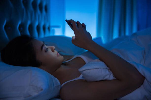 アジアの女性は、夜に眠っている彼女の前にベッドの上、スマート フォンを使用しています。携帯中毒の概念。