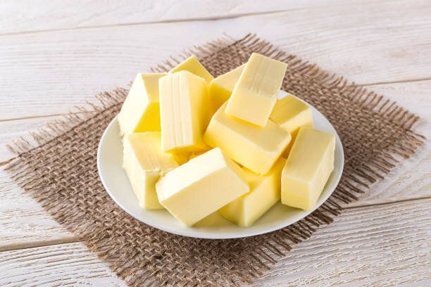 白い木製のテーブルの上に白い受け皿の上に新鮮な黄色のバターの長方形の部分。乳製品。サンドイッチバター。自然な脂肪の栄養素。