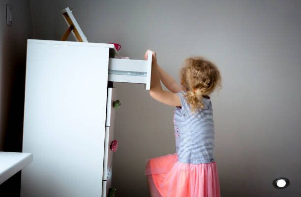 現代の高いドレッサー家具に登る若い女の子の子供、コンセプトの上にドレッサーの危険。子供の家の危険。ステージ上の写真。