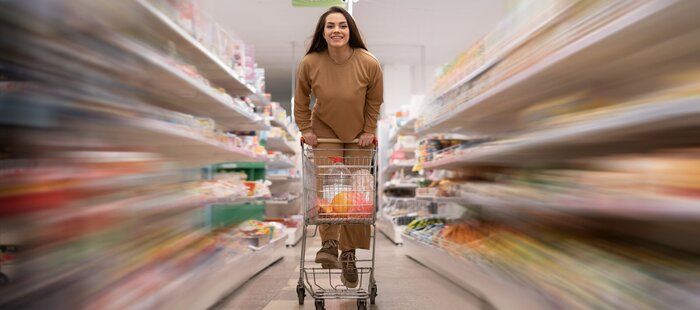 スーパーで若い白人女性。カートを押して楽しく乗ります。棚がぼやけている。買い手は食べ物を買います。