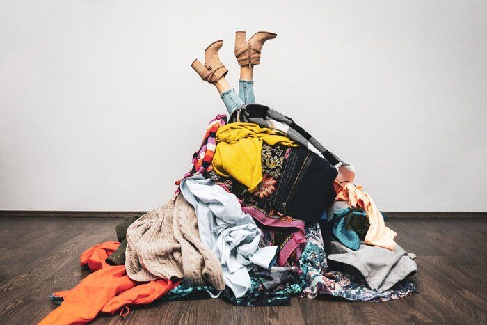 床に服の山から女性の足。ショッピング依存症の概念
